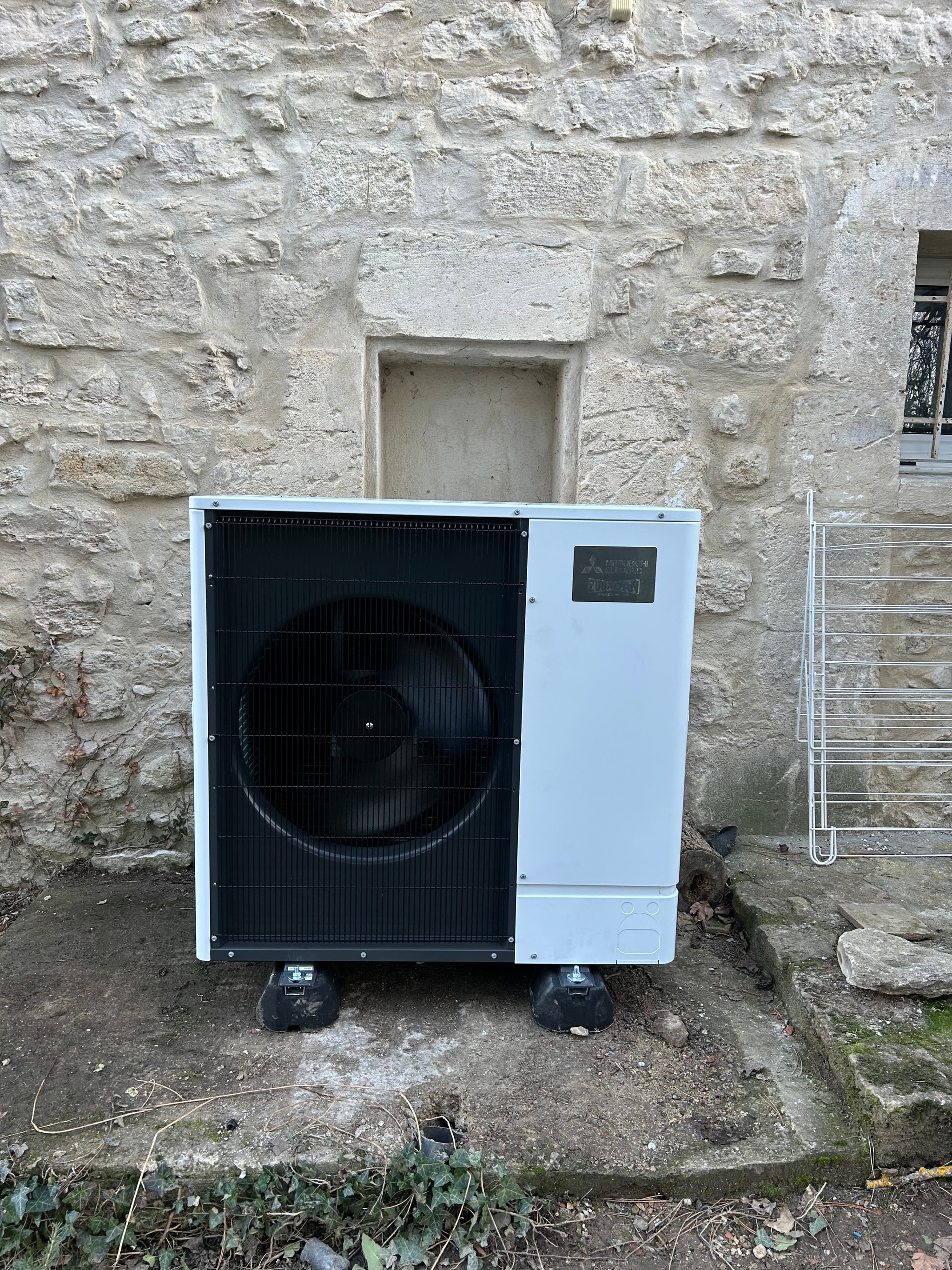 Unité extérieure de la pompe à chaleur air/eau devant la façade en pierres, seconde maison à Briançon