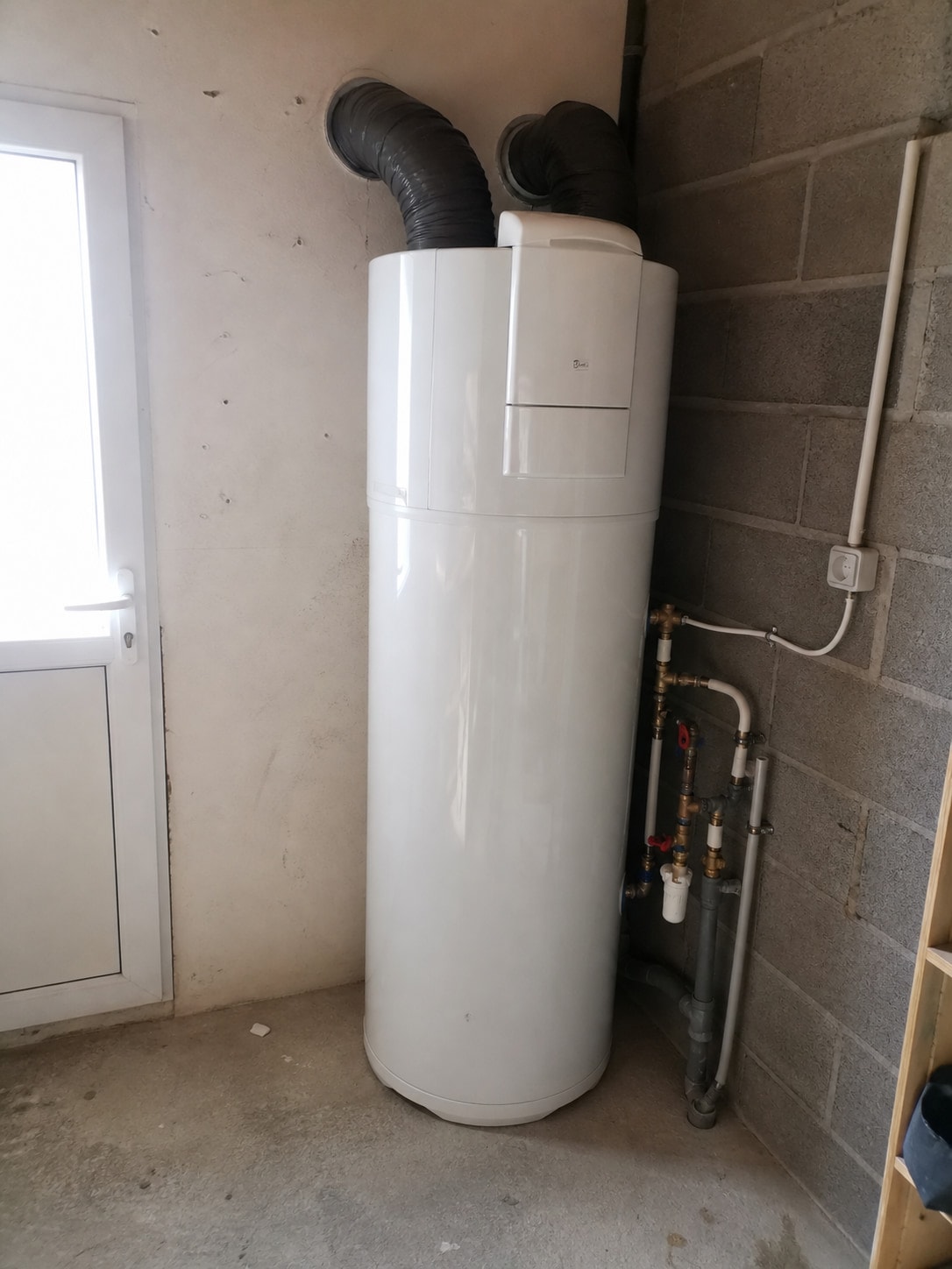 Chauffe-eau thermodynamique raccordé dans le cellier, ses deux gaines d'air isolées traversant le mur, maison à Embrun
