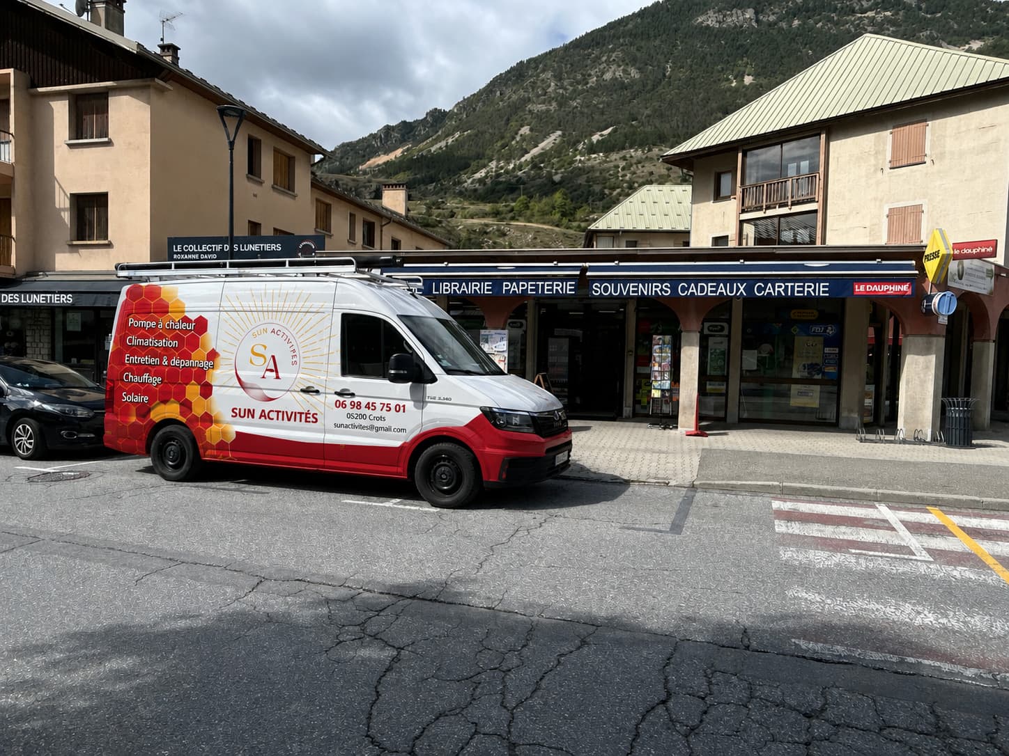 Le fourgon Sun Activités stationné devant le bureau de tabac et presse de L'Argentière-la-Bessée, la montagne au fond