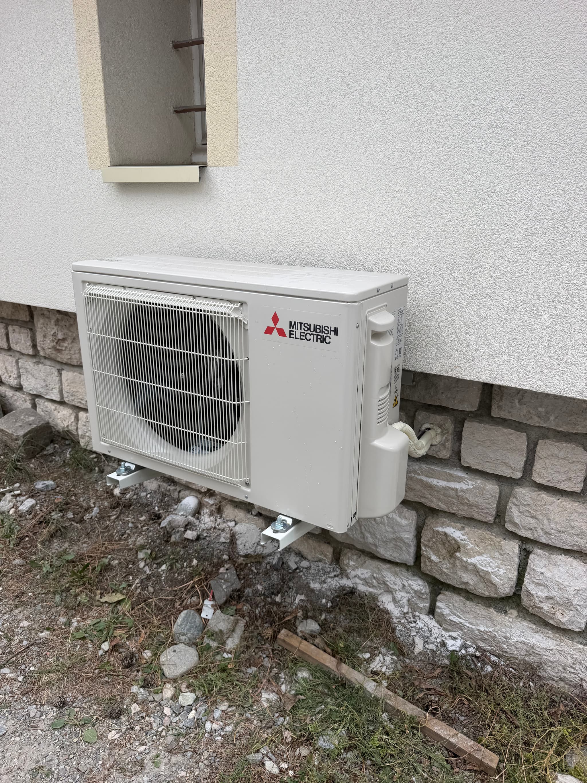 Unité extérieure fixée sur un mur crépi au-dessus d'un soubassement en pierre, appartement à Châteauroux-les-Alpes