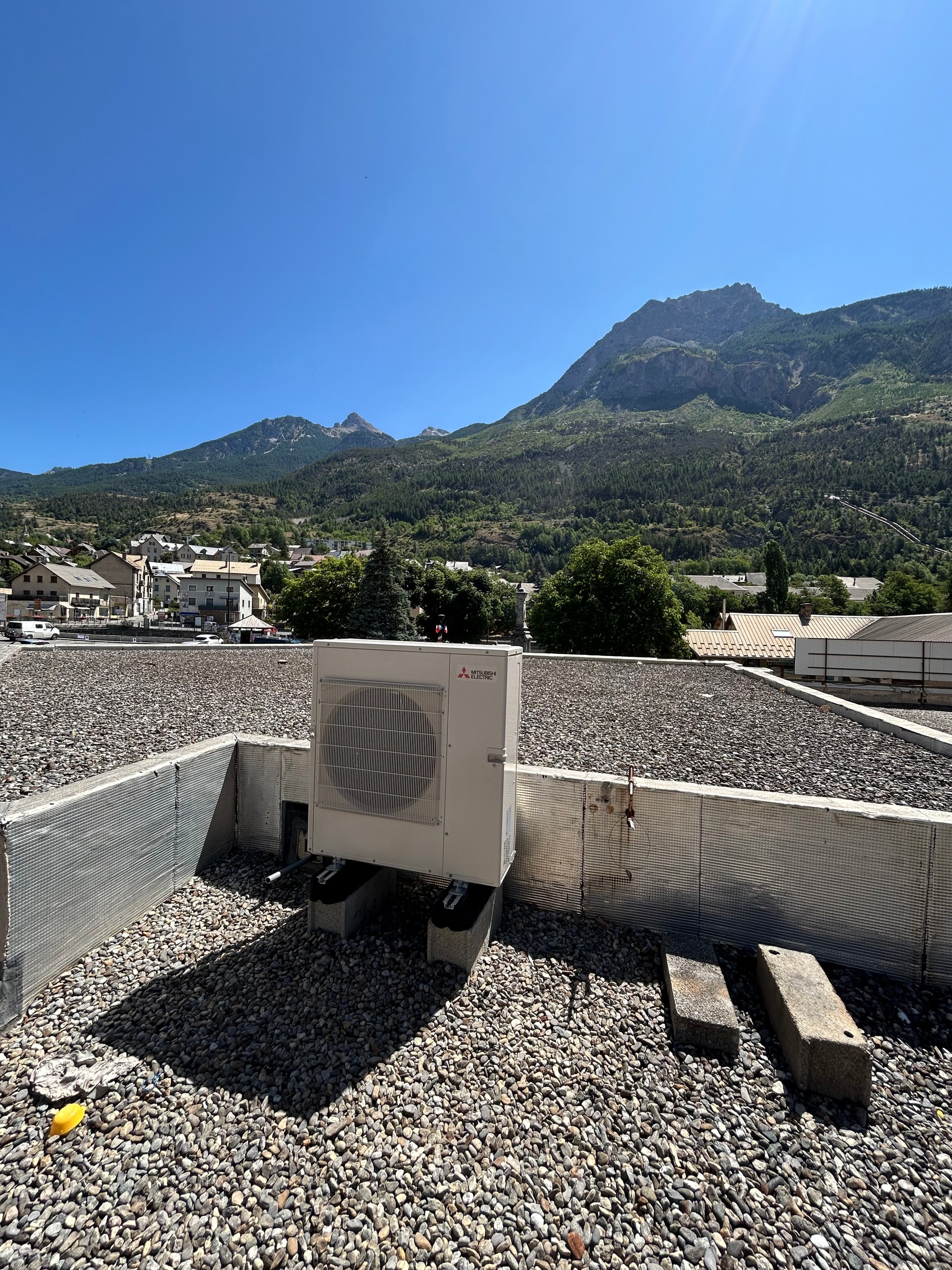Unités extérieures installées sur le toit terrasse d'un commerce à L'Argentière-la-Bessée, sommets au fond