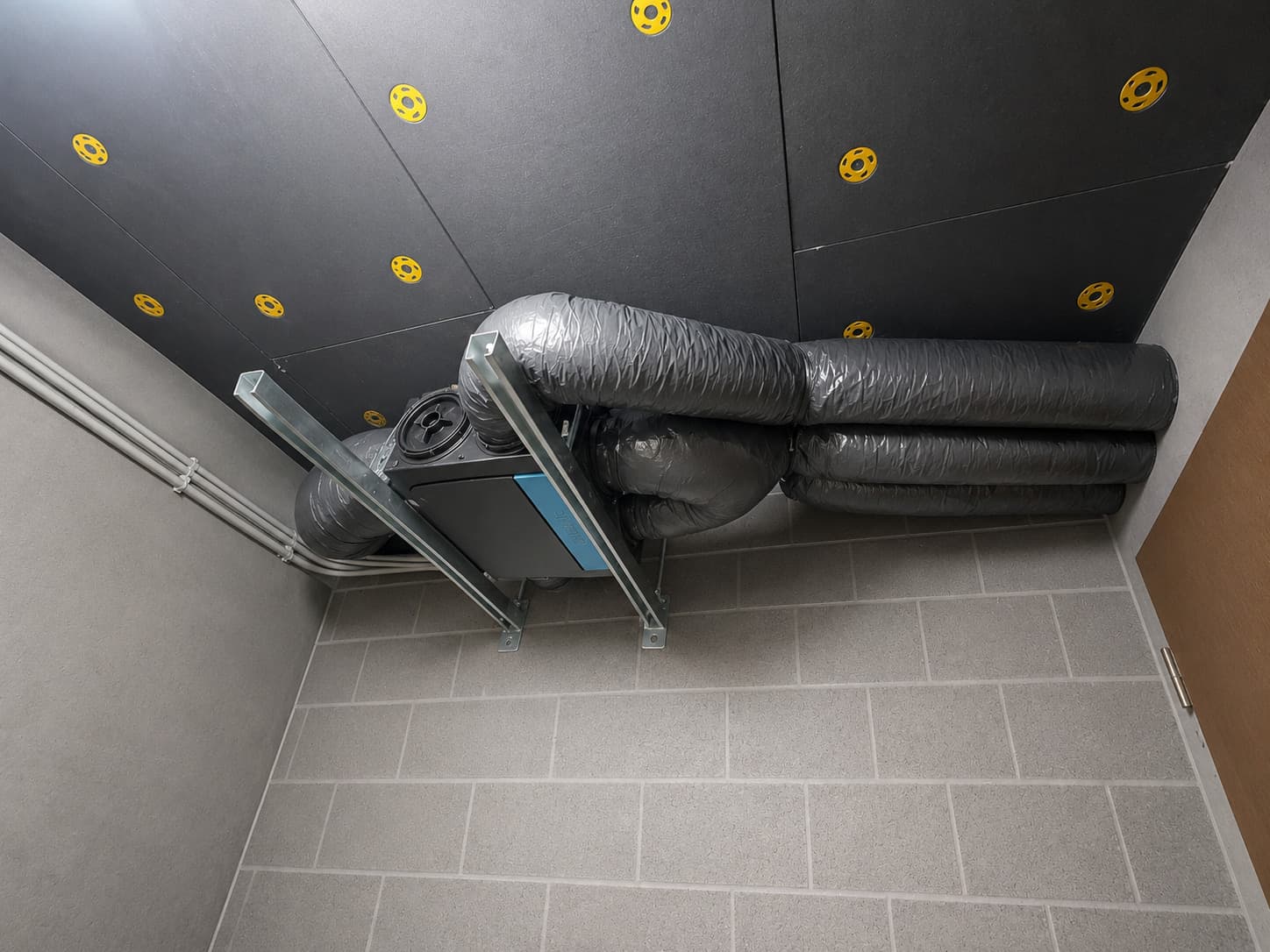 Caisson de VMC simple flux et son réseau de gaines isolées, fixé sous plafond dans le local technique d'une maison à Embrun